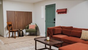 A living room with a brown sofa, a wooden chair, a green armchair, a small round table, and a patterned rug. - NEW Spacious Park-view Walk-out Basement near Coffee and Trails (Colorado Springs)