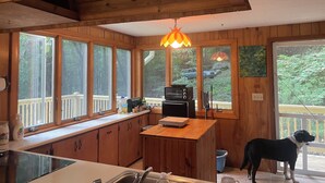 A kitchen with wooden cabinets, a microwave, a sink, and a dog standing by the door. - Charming 2-bedroom cabin in Waynesville (Waynesville)