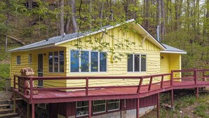 A yellow cabin with a red deck, surrounded by trees. - Charming 2-bedroom cabin in Waynesville (Waynesville)