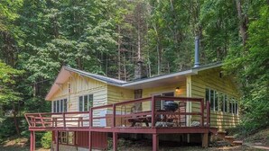 A cabin with a deck, a chimney, and a stone structure in the background. - Charming 2-bedroom cabin in Waynesville (Waynesville)