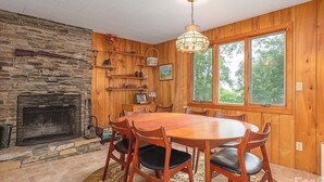 A wooden interior with a stone fireplace, a dining table with chairs, and a large window. - Charming 2-bedroom cabin in Waynesville (Waynesville)