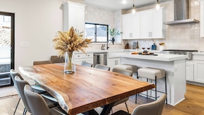 A modern kitchen with white cabinets, a wooden dining table, and a vase with dried flowers. - Hot Tub, BBQ & Mtn Views Near Deer Valley & Park City Deer Valley East Retreat by Avantstay (Heber City)