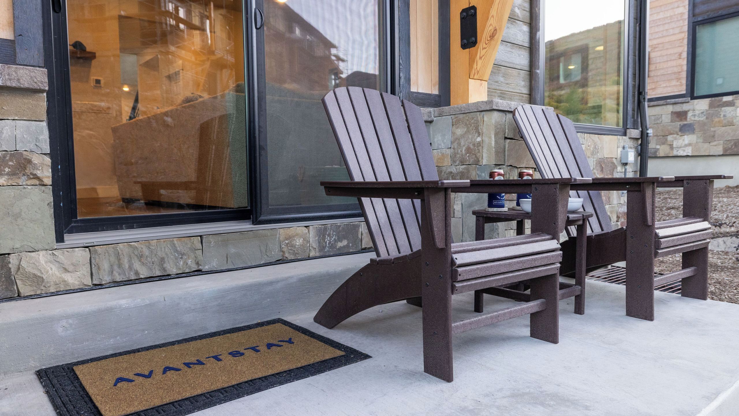 Deux fauteuils Adirondack sont placés à l’extérieur, devant un bâtiment à la façade en pierre et doté de grandes fenêtres.