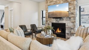 Ett modernt vardagsrum med en stenbeklädd öppen spis, läderfåtöljer, ett runt soffbord och en stor platt-TV som är monterad på en stenbeklädd vägg.