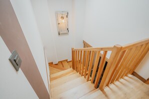 A wooden staircase with a handrail, a light switch on the wall, and a door with a light fixture above it.