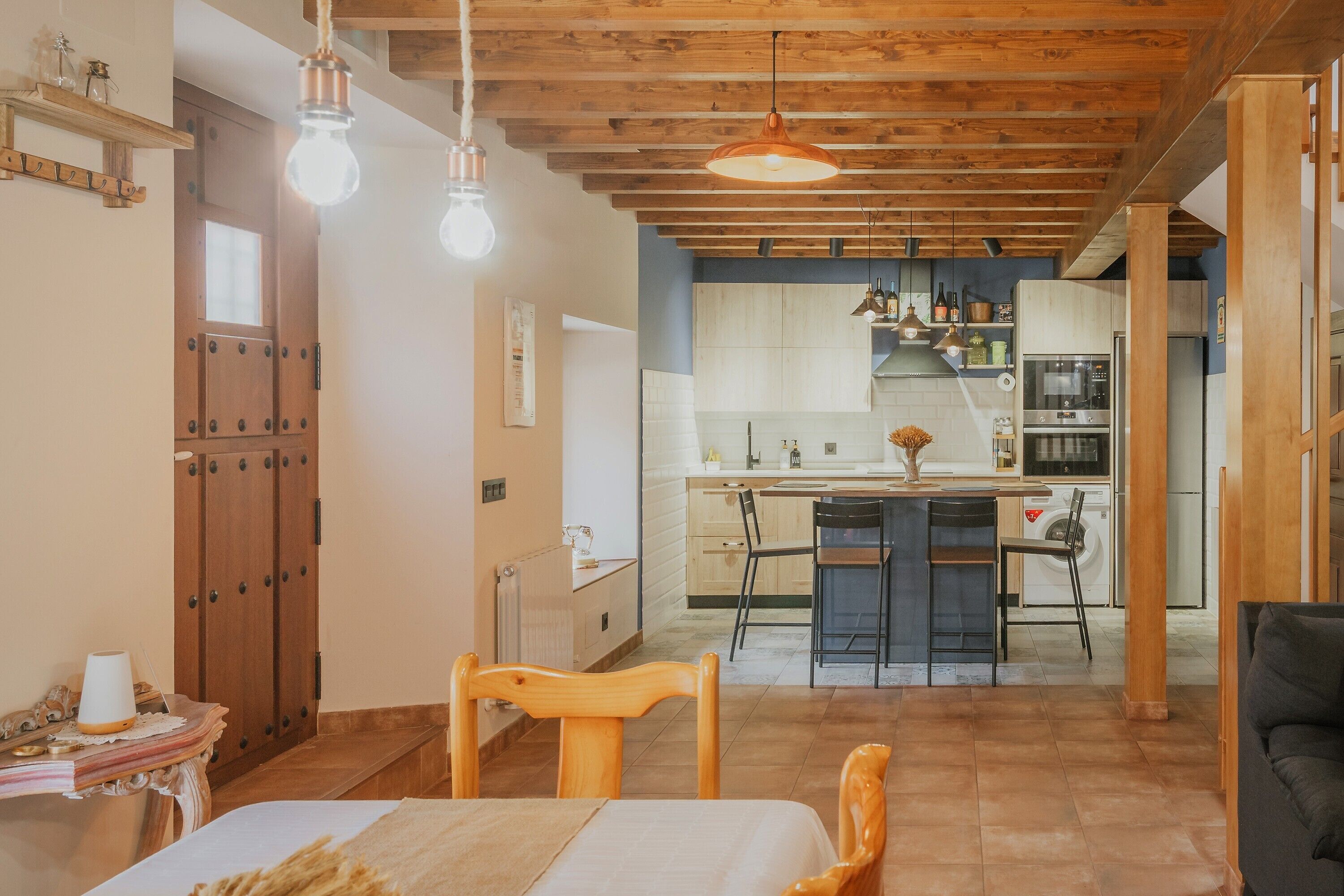 A room with a bed, wooden furniture, a table, and a kitchen in the background.