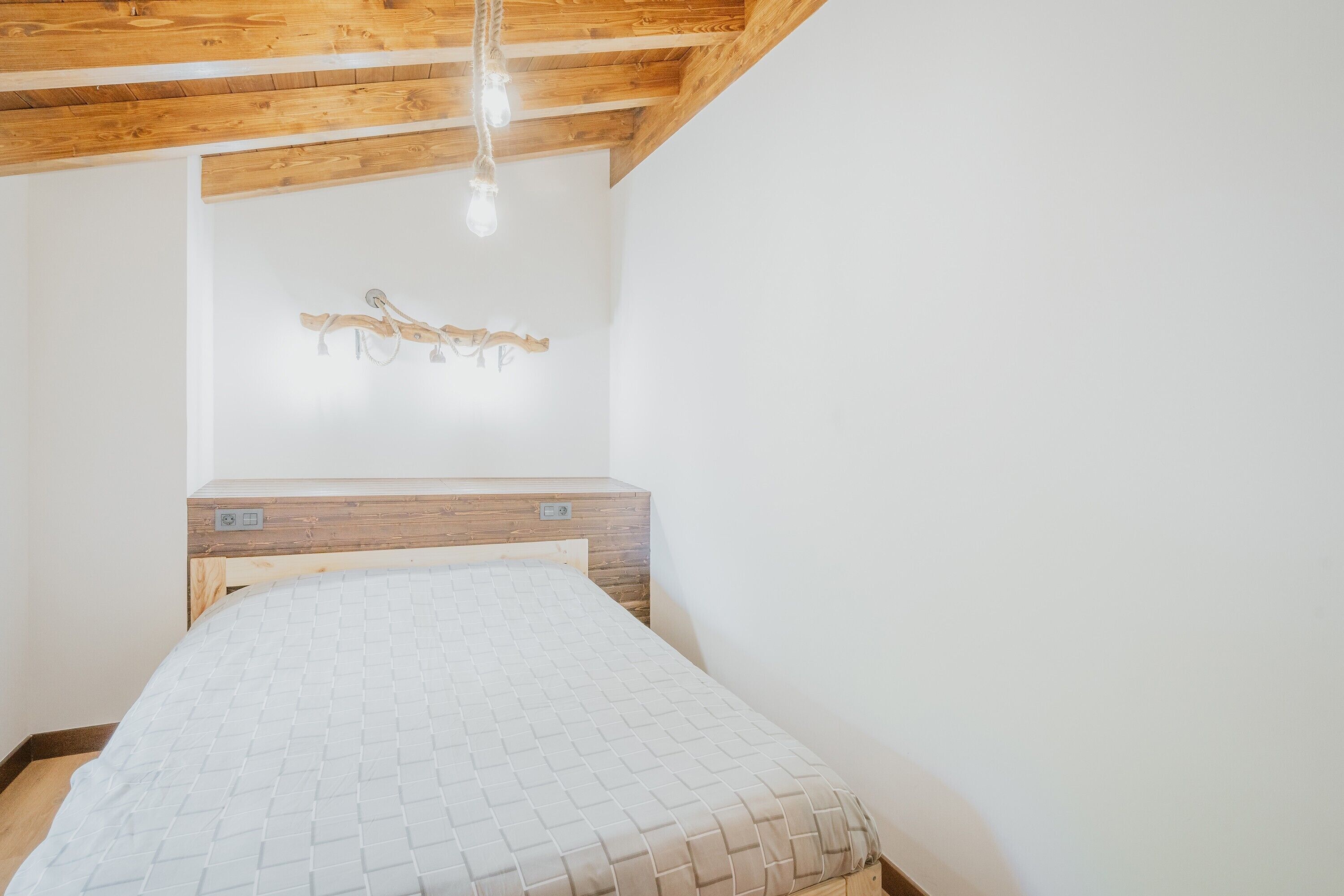 A bedroom with a wooden headboard, a bed with a quilted cover, and a wall-mounted light fixture.