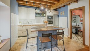 A kitchen with a central island, wooden ceiling beams, and a tiled floor. - El Rinconcito de Cinderellana – Rural House in Sierra de la Demanda (La Revilla)