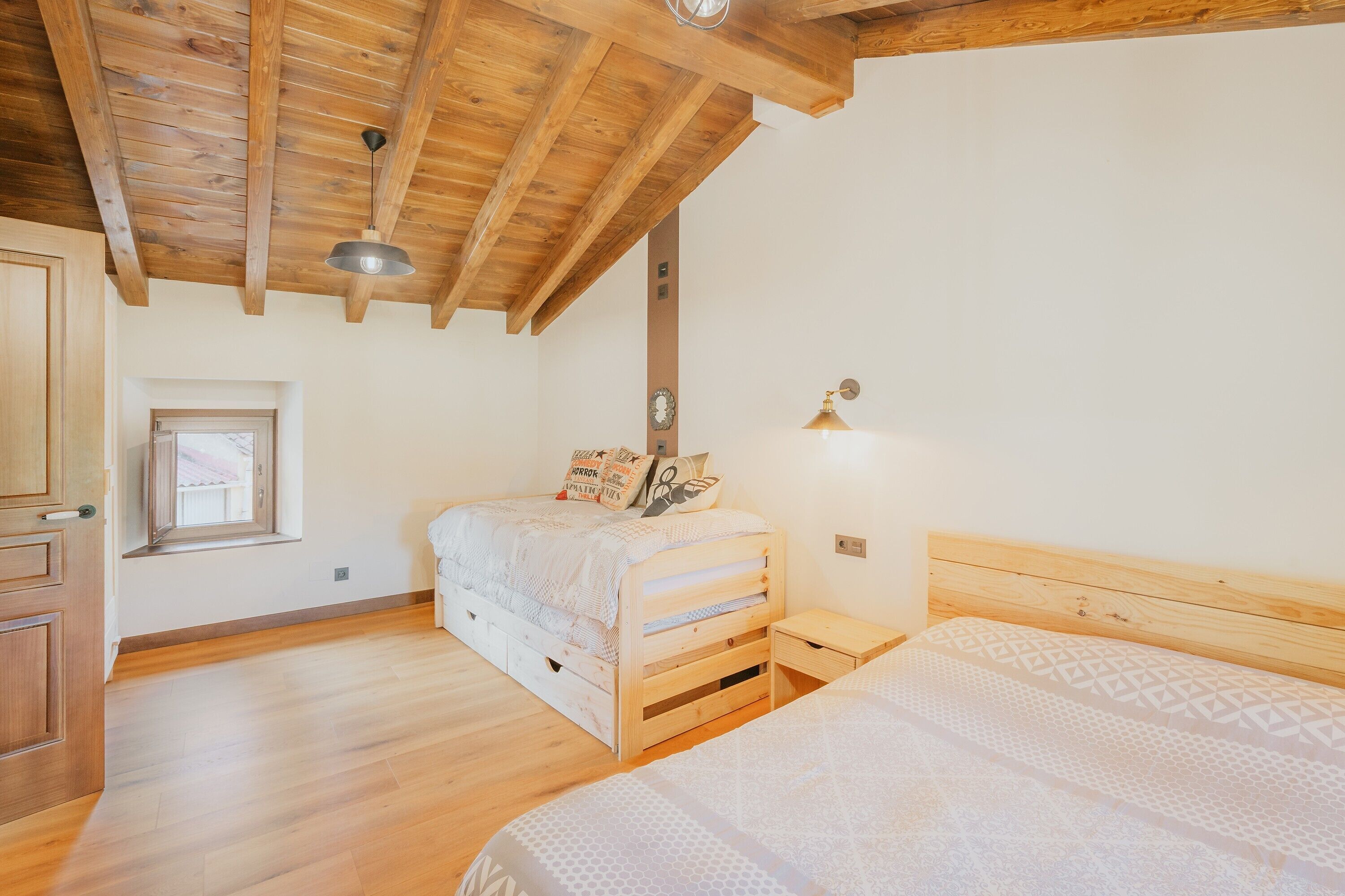 Een slaapkamer met houten balken, een bed, een nachtkastje, een raam en een wandklok.