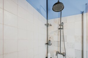 A shower with a handheld showerhead, a wall-mounted faucet, and a soap dispenser.