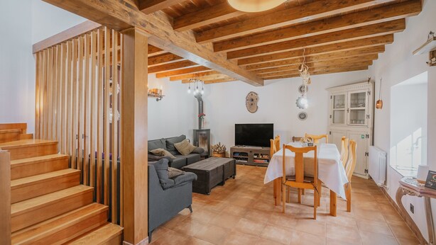A spacious living area with a wooden staircase, a sofa, a TV, and a dining table with chairs. - El Rinconcito de Cinderellana – Rural House in Sierra de la Demanda (La Revilla)