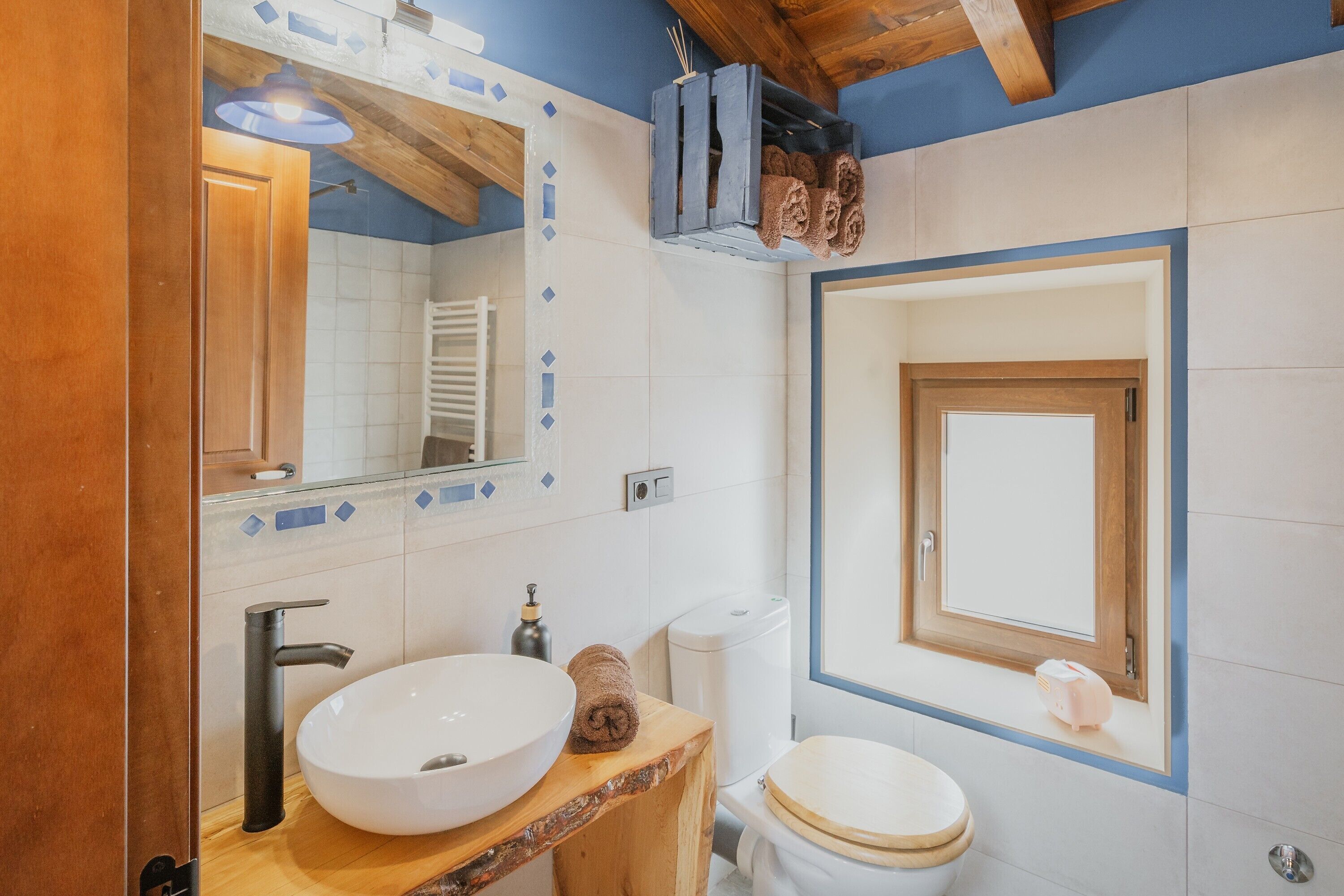 Een badkamer met een houten wastafelmeubel, een witte wastafel, een toilet en een spiegel.