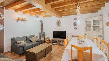 Una sala de estar con sofá, mesa de centro de madera, televisor y comedor con sillas y una mesa.