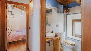Un dormitorio con cama, baño con lavamanos, inodoro y ventana.