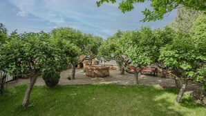 A courtyard with trees, a stone fountain, and a red cart. - El Rinconcito de Cinderellana – Rural House in Sierra de la Demanda (La Revilla)