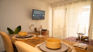 A dining area with a wooden table, two bowls, two wine glasses, and a television mounted on the wall. - Cocon Chic  Res de Charme (Cayenne)