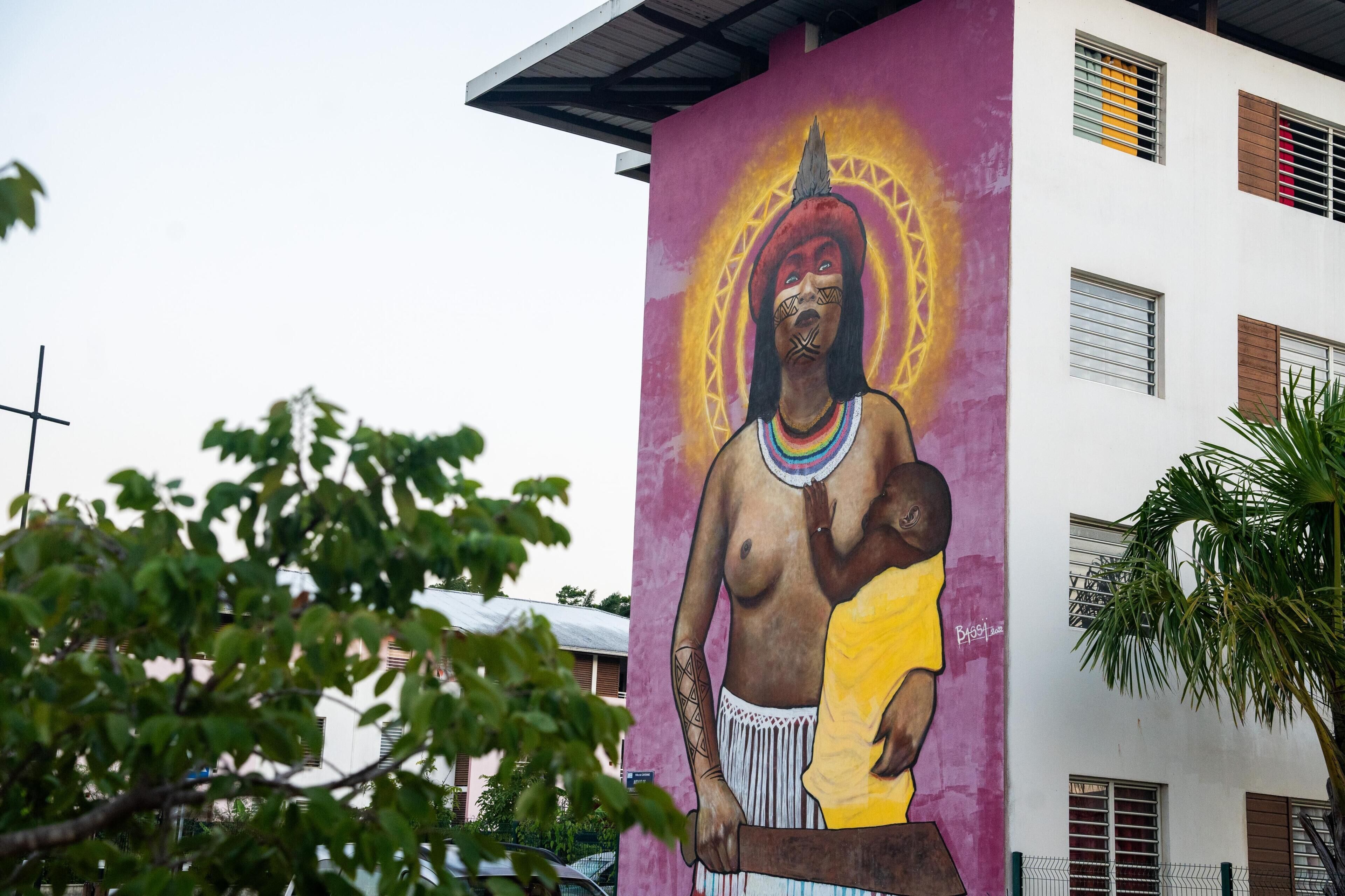 A mural of a figure on a building with a cross, windows, and a tree.