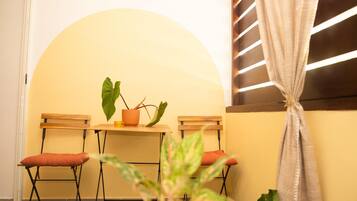 Una habitación pequeña con una mesa, dos sillas, una planta en maceta y una cortina.