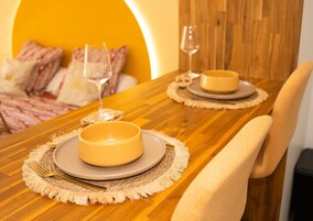 Uma mesa de jantar posta com pratos, talheres e copos, com uma cadeira posicionada ao lado.