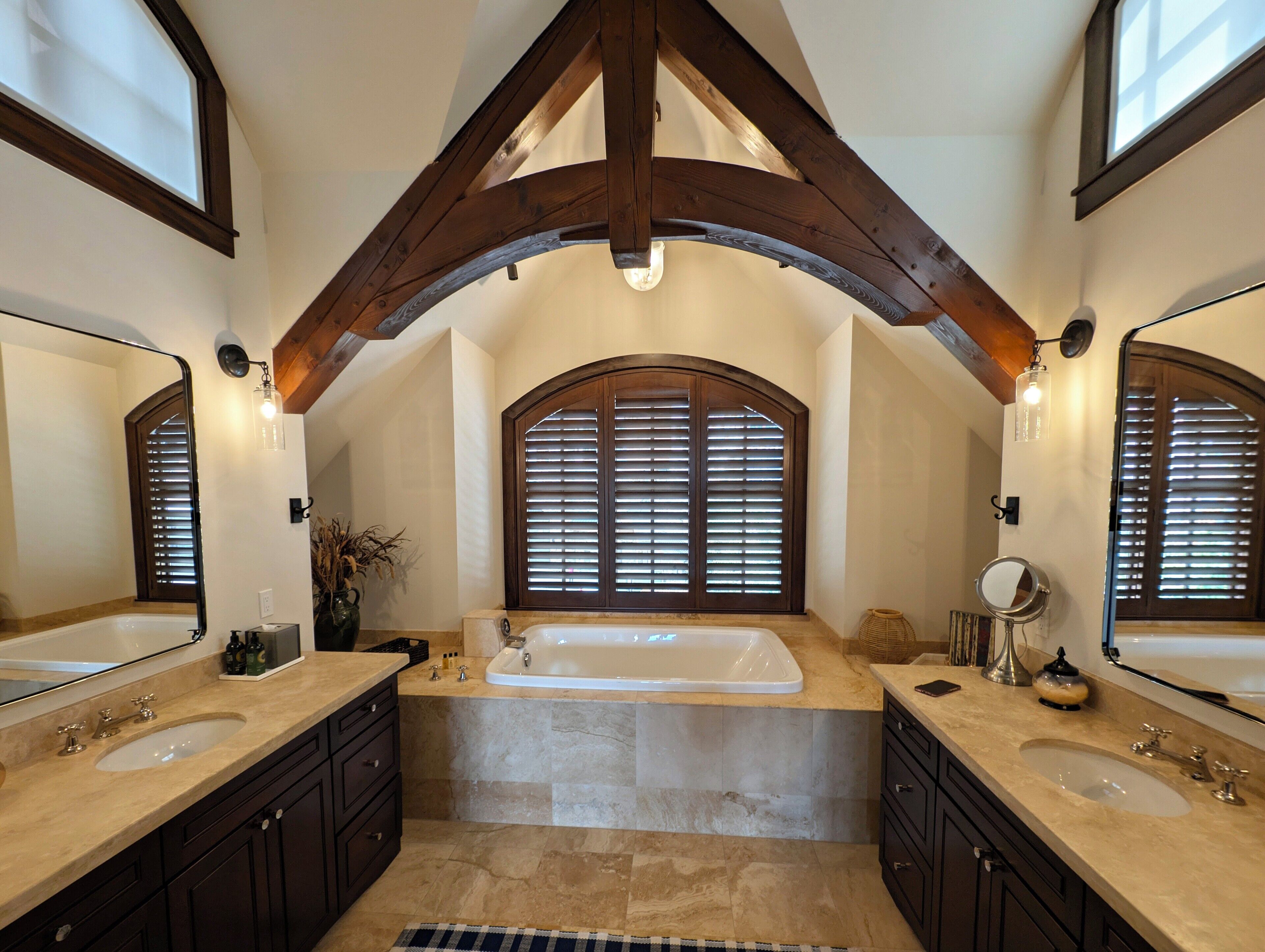 A spacious bathroom with two sinks, a large bathtub, and a window with blinds.