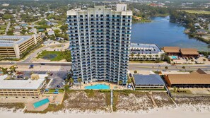 A high-rise hotel with multiple balconies, a pool, and a view of the surrounding area including a beach and a body of water. - 2 Beachfront Condos BBQ Balconies, Resort Pool, Hot Tub + Direct Beach Access (Panama City Beach)