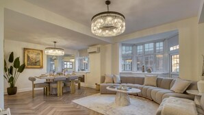 A spacious living room with a large sofa, a dining area with a table and chairs, and a chandelier.