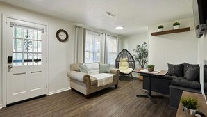 Un salon comprenant un canapé beige, un canapé gris foncé, un fauteuil rond, une petite table avec une plante, et une étagère murale ornée de deux plantes en pot.