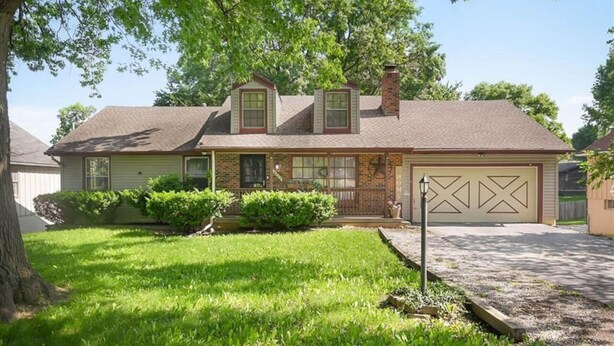 Une maison à deux étages avec un garage à l’avant, une pelouse bien entretenue et de grands arbres.