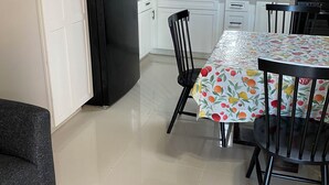 A modern kitchen with white cabinets, a black refrigerator, and a dining area with a table covered in a fruit-patterned tablecloth.