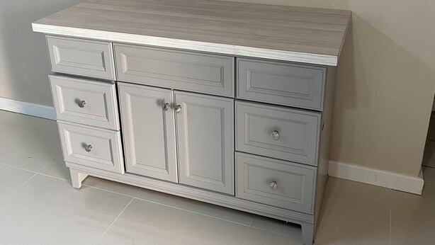 A light grey wooden cabinet with drawers and doors, positioned against a plain wall with a white baseboard.