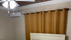 A neatly made bed with white linens, a wooden headboard, and a beige curtain.