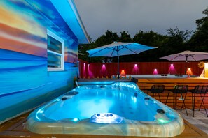 A hot tub with a window, outdoor seating, and a red fence in the background.