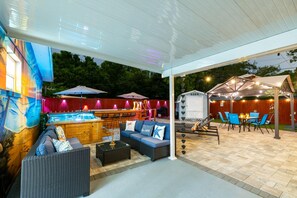 An outdoor patio area with a covered seating area, a hot tub, and a bar.