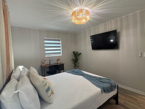 A bedroom with a bed, a desk, a television, and a ceiling light fixture.