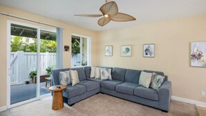 A living room with a sectional sofa, a round wooden coffee table, and a ceiling fan. - Modern Family Beach Villa near shops and dining (Kapolei)