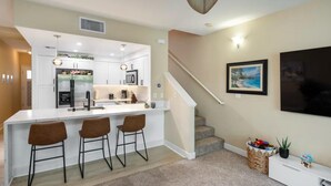A modern kitchen with a central island, bar stools, and a staircase leading to another level. - Modern Family Beach Villa near shops and dining (Kapolei)