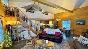 A cozy cabin interior with a wooden staircase, a dining area, and a living room furnished with a leather sofa and a coffee table. - Waterfront Log Cabin on Airstrip with Aurora Views (Fairbanks)
