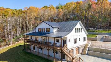 A large white house with a covered porch and a staircase leading to a deck.