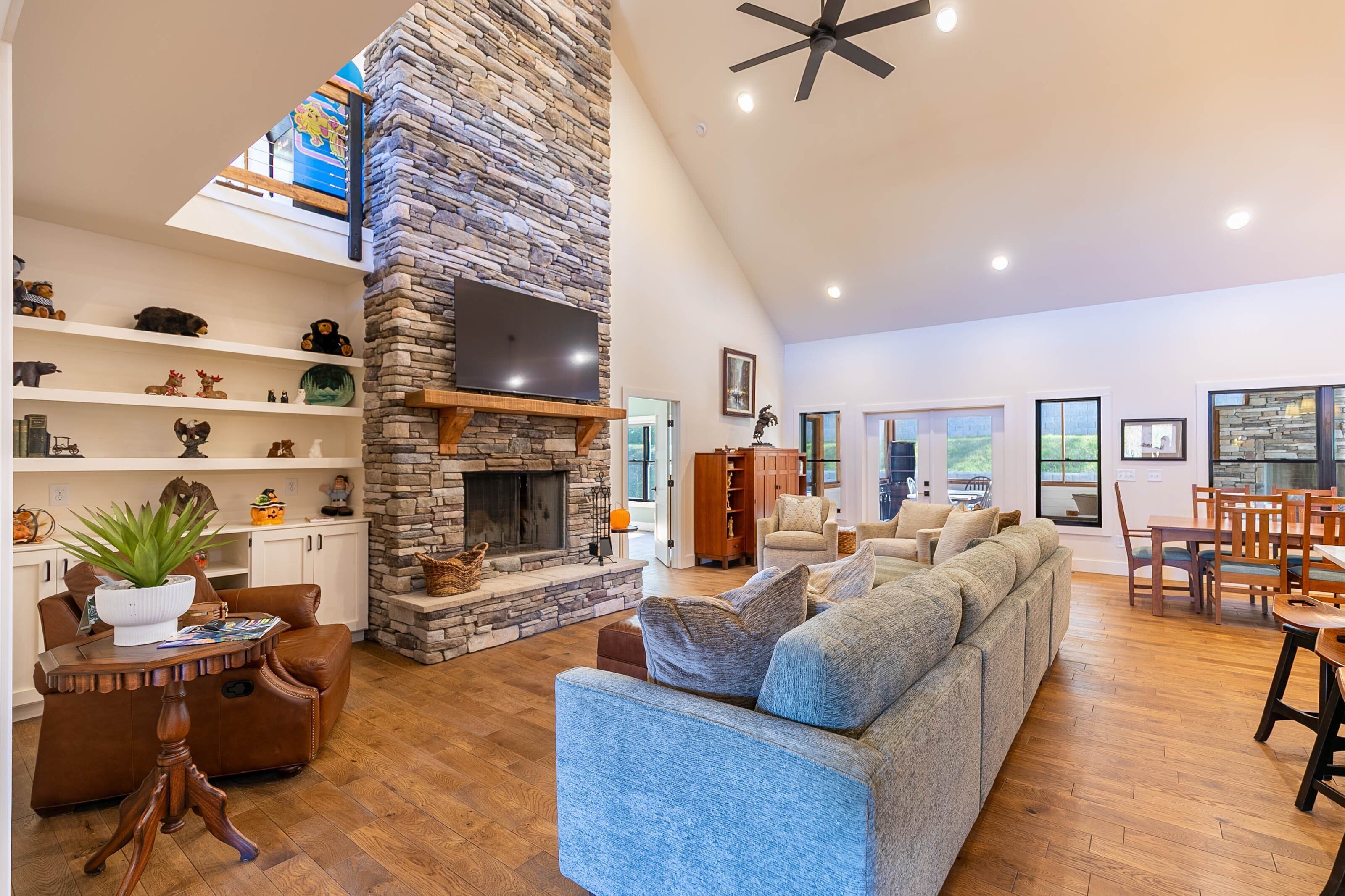 A spacious living room with a stone fireplace, a large sectional sofa, and a dining area with wooden furniture.