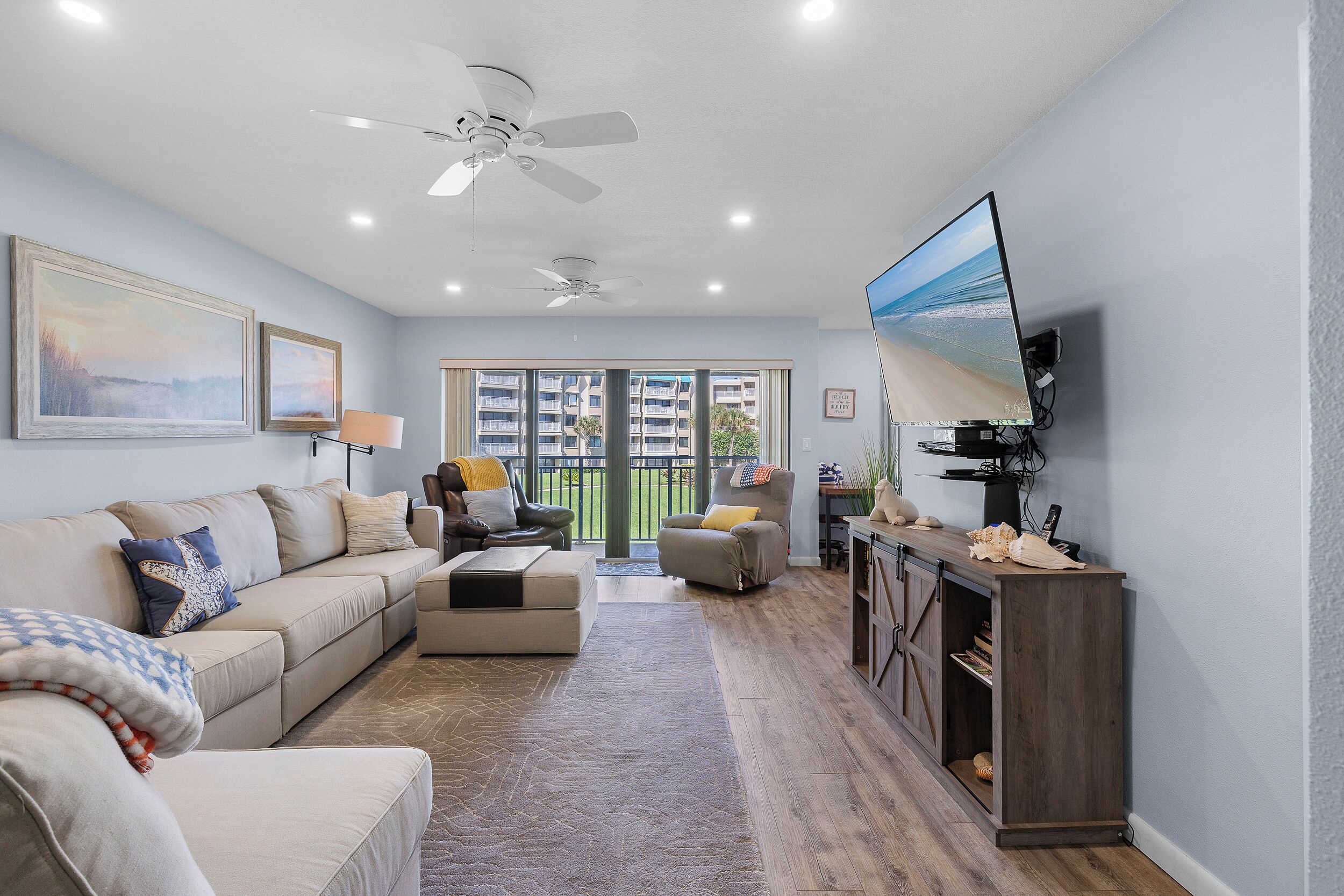 A spacious living room with a beige sofa, a coffee table, and a TV mounted on the wall.