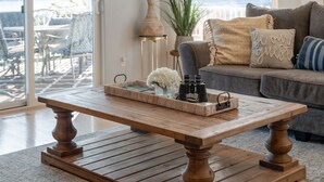 A wooden coffee table with a tray, a potted plant, and decorative pillows in a living room with a view of the outdoors. - Summerset Poolside Paradise (Manson)