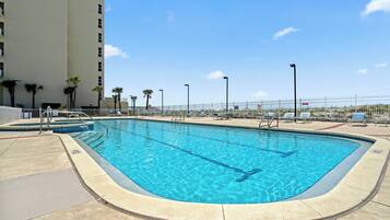 A rectangular swimming pool with clear blue water, surrounded by a white fence, and adjacent to a multi-story building.