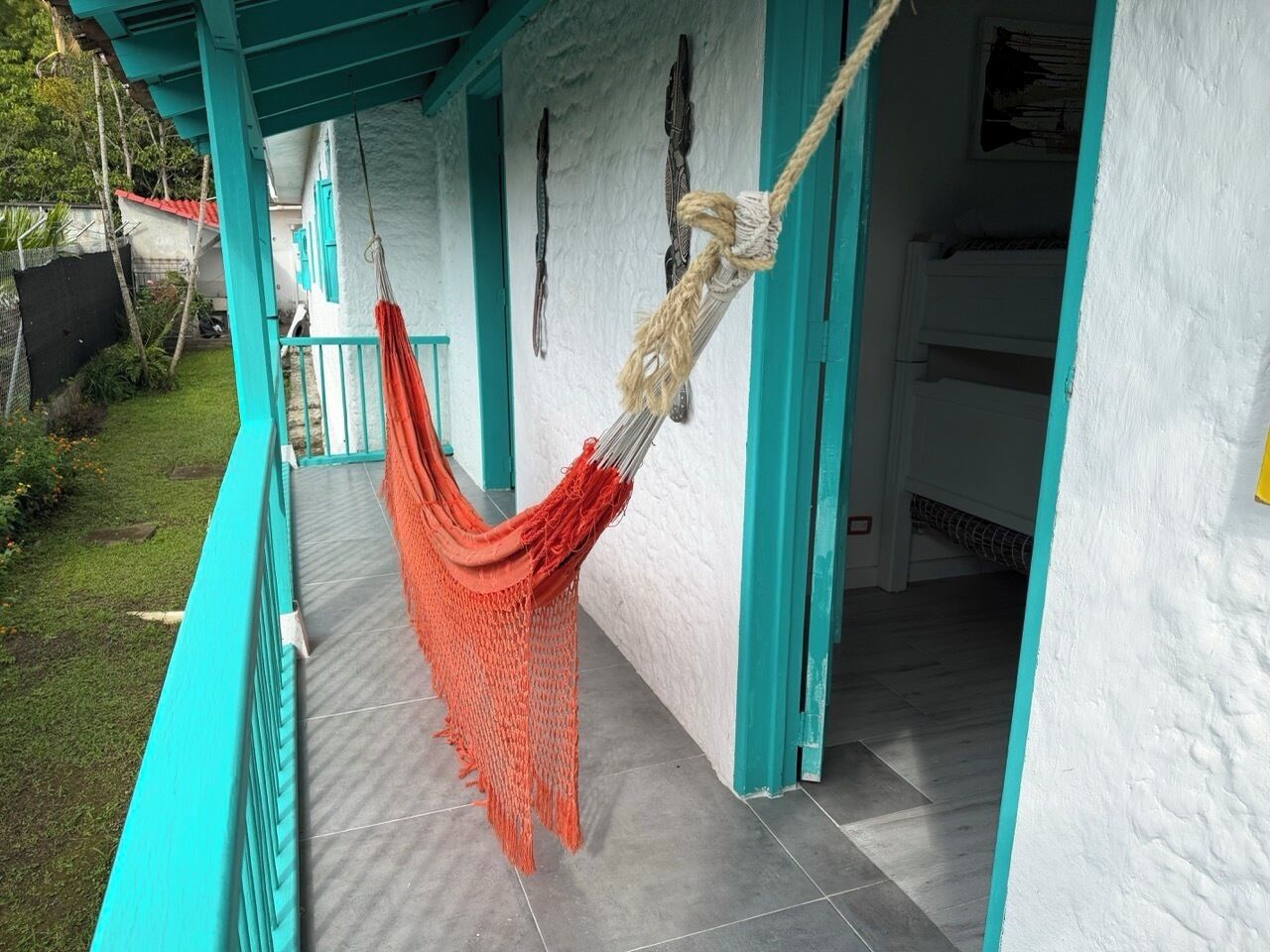 A hammock hanging from a balcony with a white wall and teal accents.