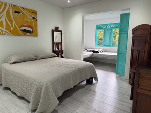 A bedroom with a bed, a mirror, a wooden dresser, and a window with a teal door.