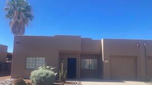 A modern building with a flat roof, a front door, and a garage. There are cacti and a palm tree in the front yard. - 55+ 2-bedroom, 2-bathroom Townhouse in The Springs at Santa Rita of Green Valley (The Springs At Santa Rita, Green Valley)