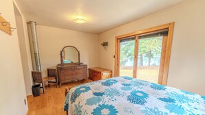 Un dormitorio con cama, cómoda de madera, espejo y ventana con vistas a árboles.