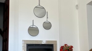 Una sala de estar moderna con chimenea, tres espejos colgados en la pared, un jarrón azul con ramas y un arreglo floral rojo.