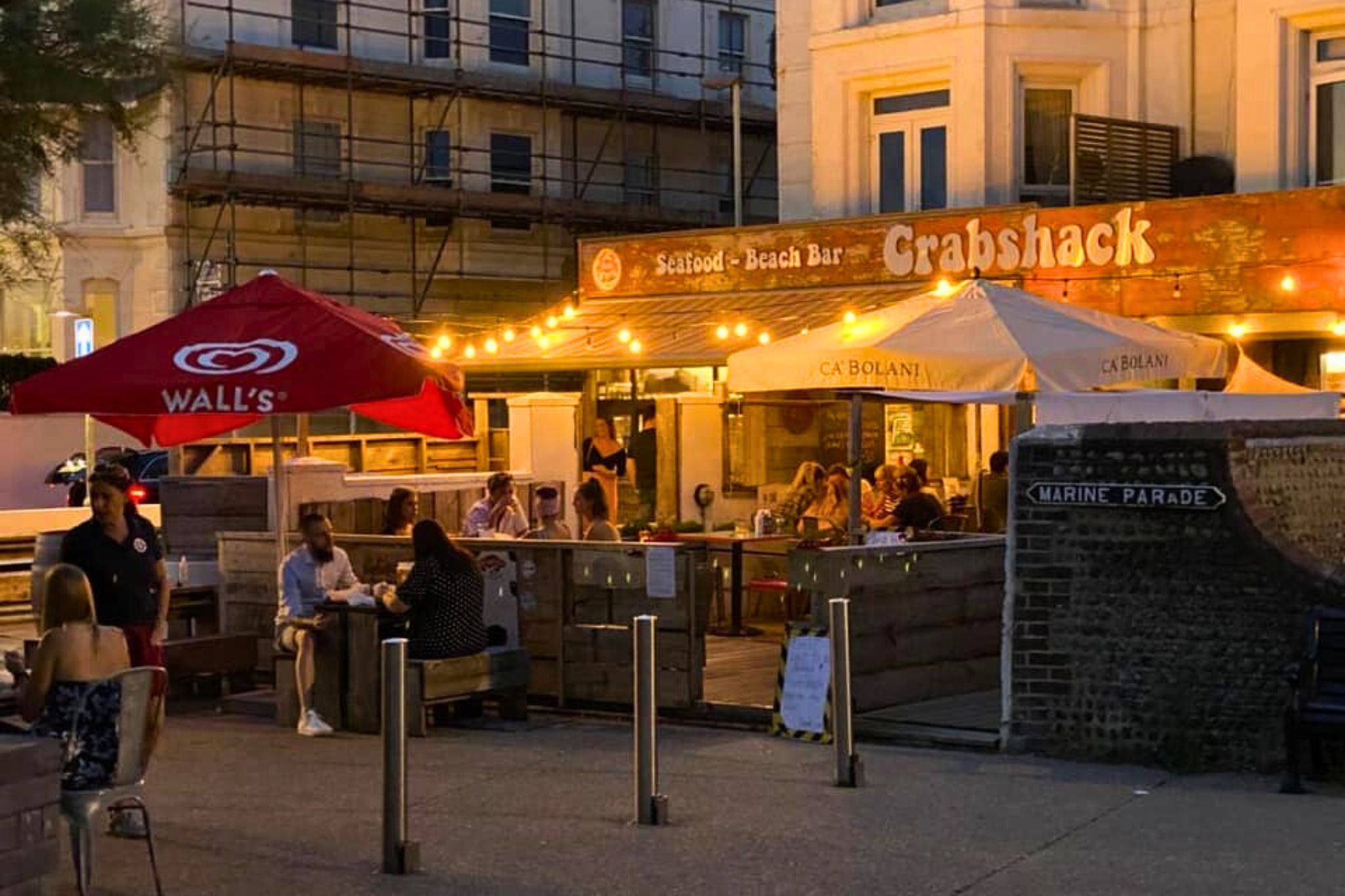 A waterfront restaurant named Crabshack with outdoor seating and a sign for a marine parade.