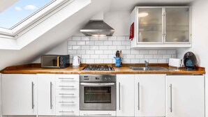A kitchen with a skylight, white cabinets, a stainless steel range hood, a microwave, a toaster, a kettle, and a sink. - Seasalt Retreat By My Getaways (Worthing)