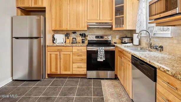 Una cocina con armarios de madera, electrodomésticos de acero inoxidable y encimera de granito.